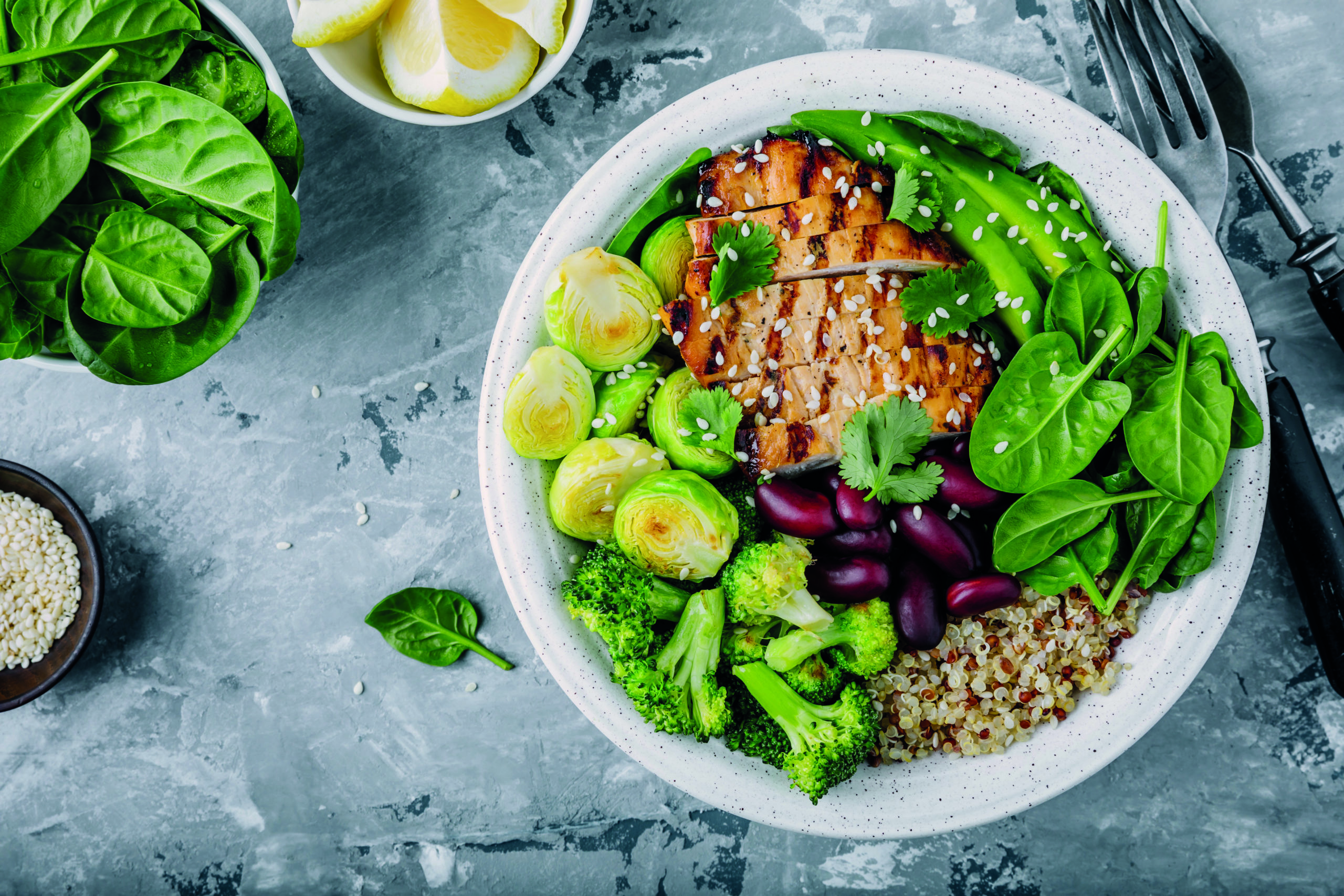 Healthy buddha bowl lunch with grilled chicken, quinoa, spinach, avocado, brussels sprouts, broccoli, red beans with sesame seeds